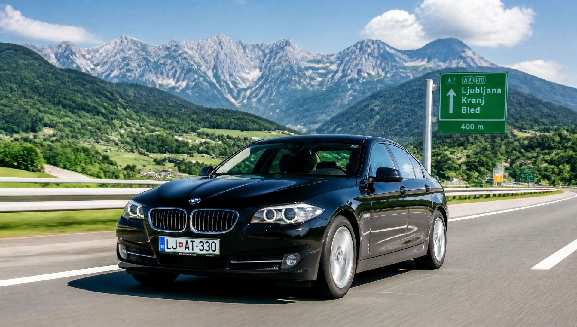 Črn BMW serije 5 na avtocesti proti Ljubljani z Alpami v ozadju
